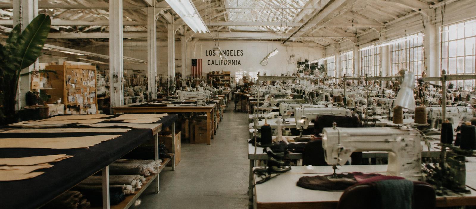 Wide view of a Los Angeles apparel factory floor with rows of sewing machines and cutting tables under natural light.